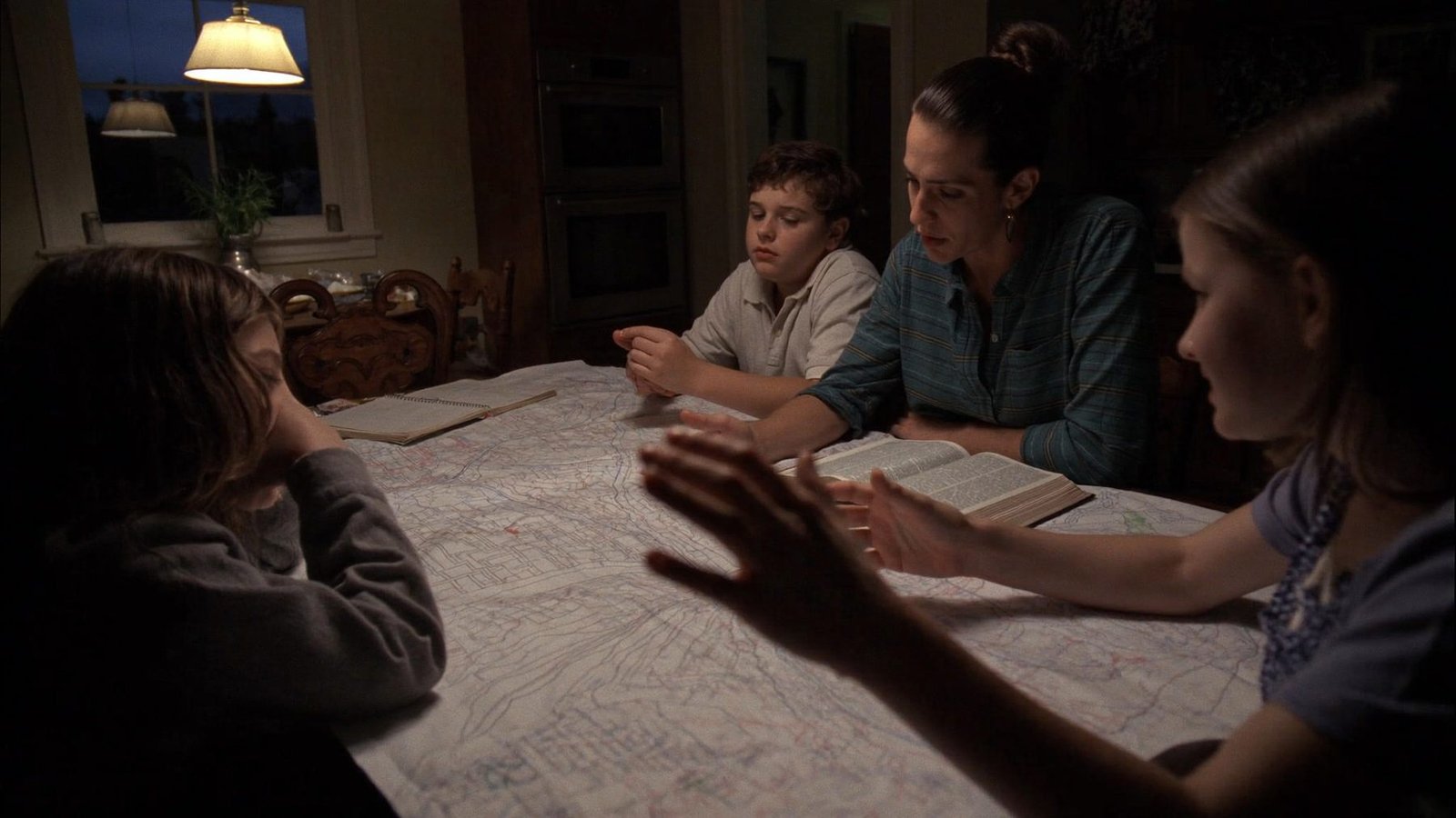 A family talking around a kitchen table with a hand-drawn map, a Bible and a notebook