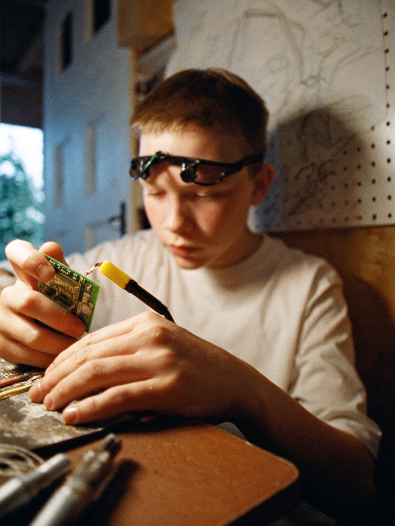 A teenager soldering a circuit board in a home workshop